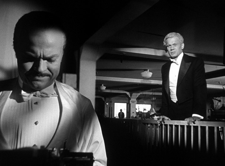 Le critique Leland (Joseph Cotten) s'approche de Kane (Orson Welles) tapant son article assassin, tandis que Bernstein (Everett Sloane) les observe dans l'encadrement de la porte.